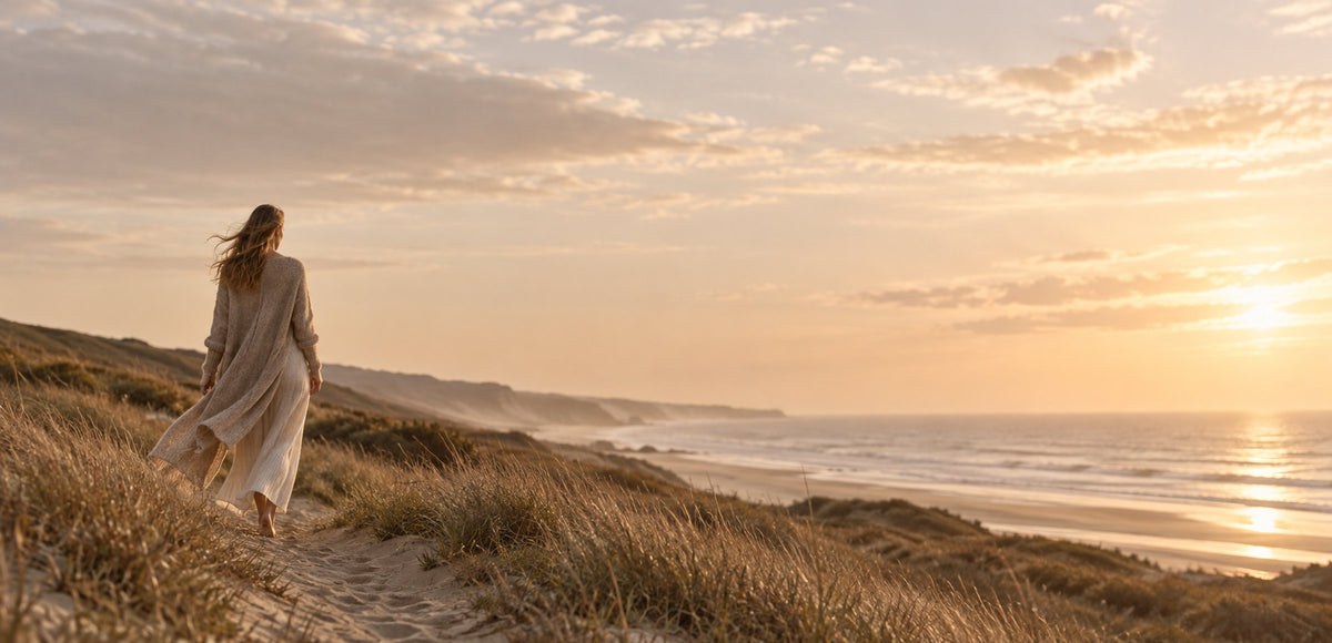 Woman in a long knit cardigan walking along the coast at golden hour